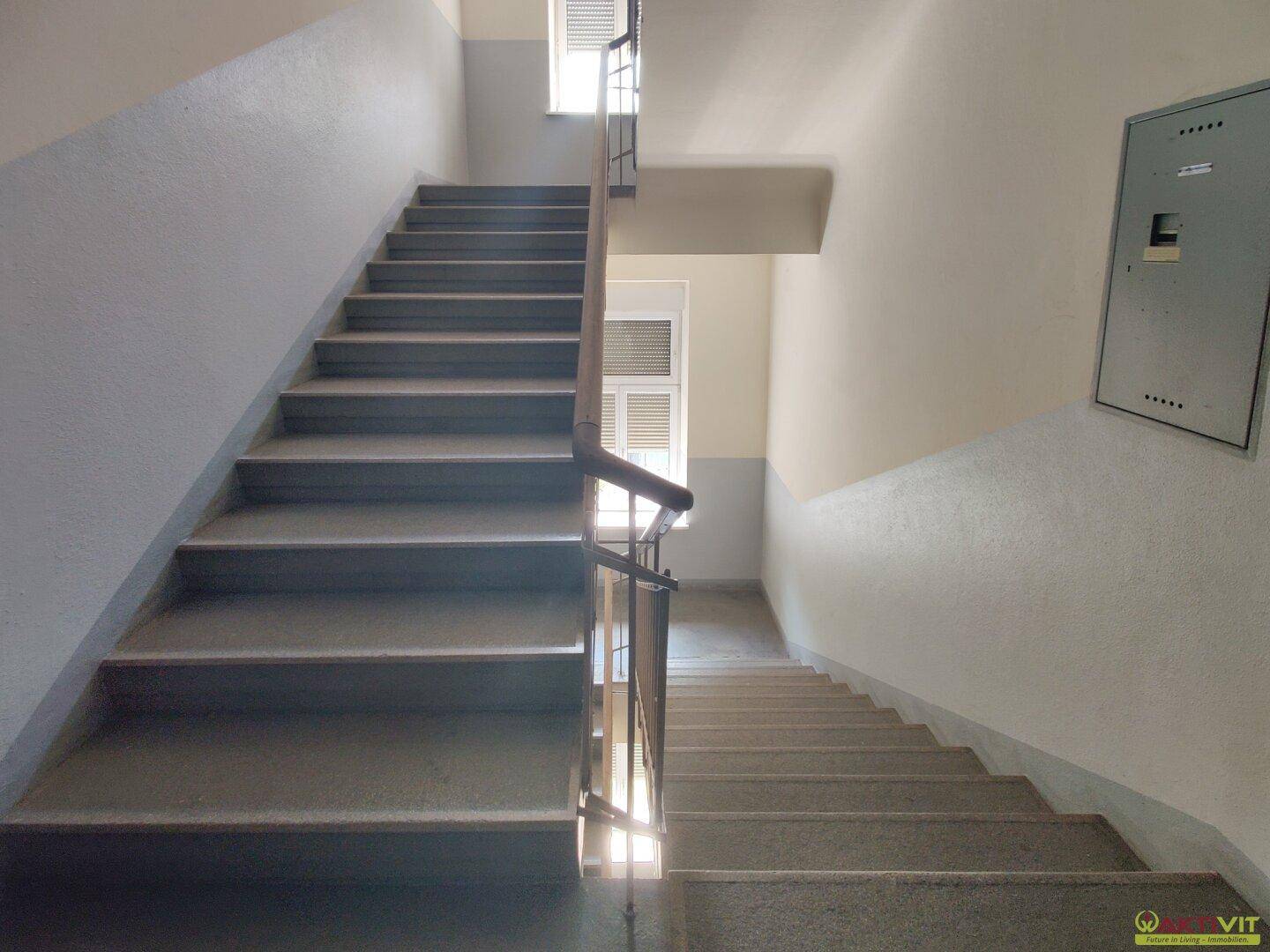 Treppenhaus eines Mehrfamilienhauses mit robusten Stufen und Fenstern für Tageslicht.
