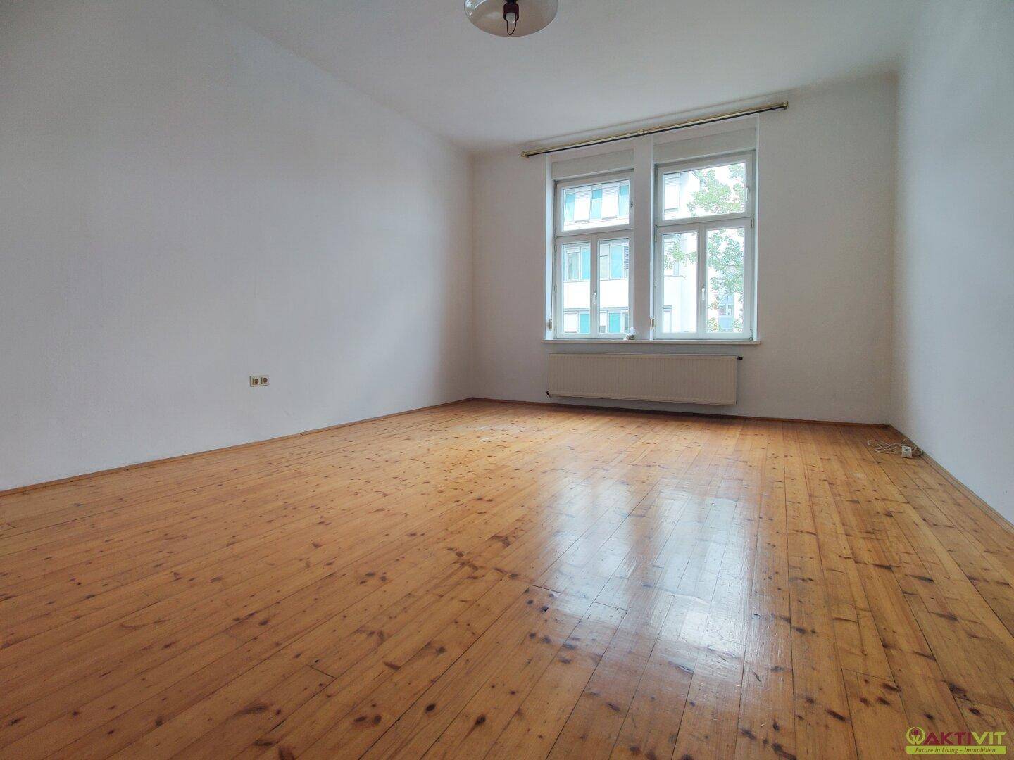 Geräumiges, helles Zimmer mit Holzdielenboden und zwei Fenstern, die eine angenehme Atmosphäre schaffen.