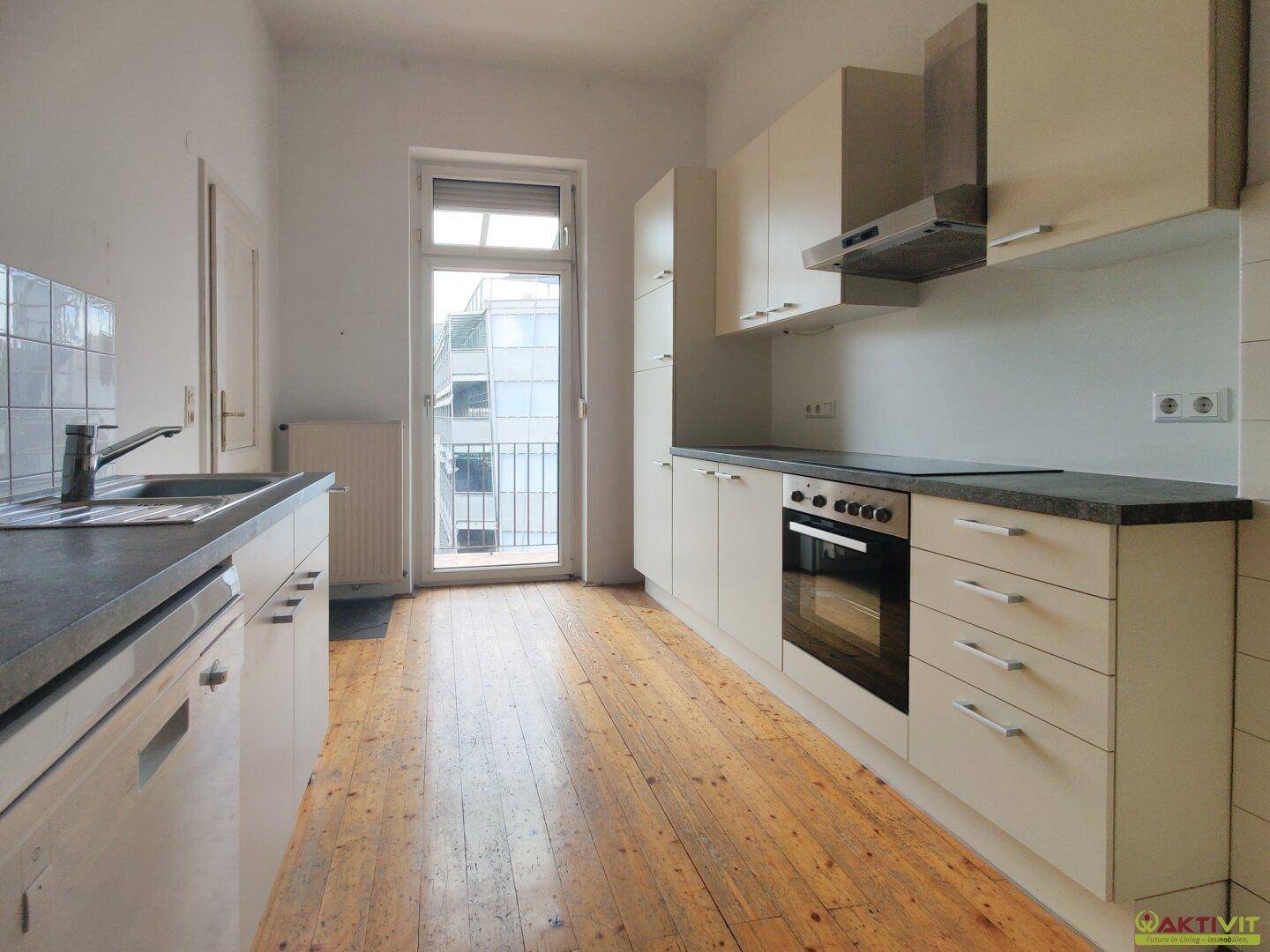 Helle Einbauküche mit cremefarbenen Schränken, dunkler Arbeitsplatte und Zugang zum Balkon.