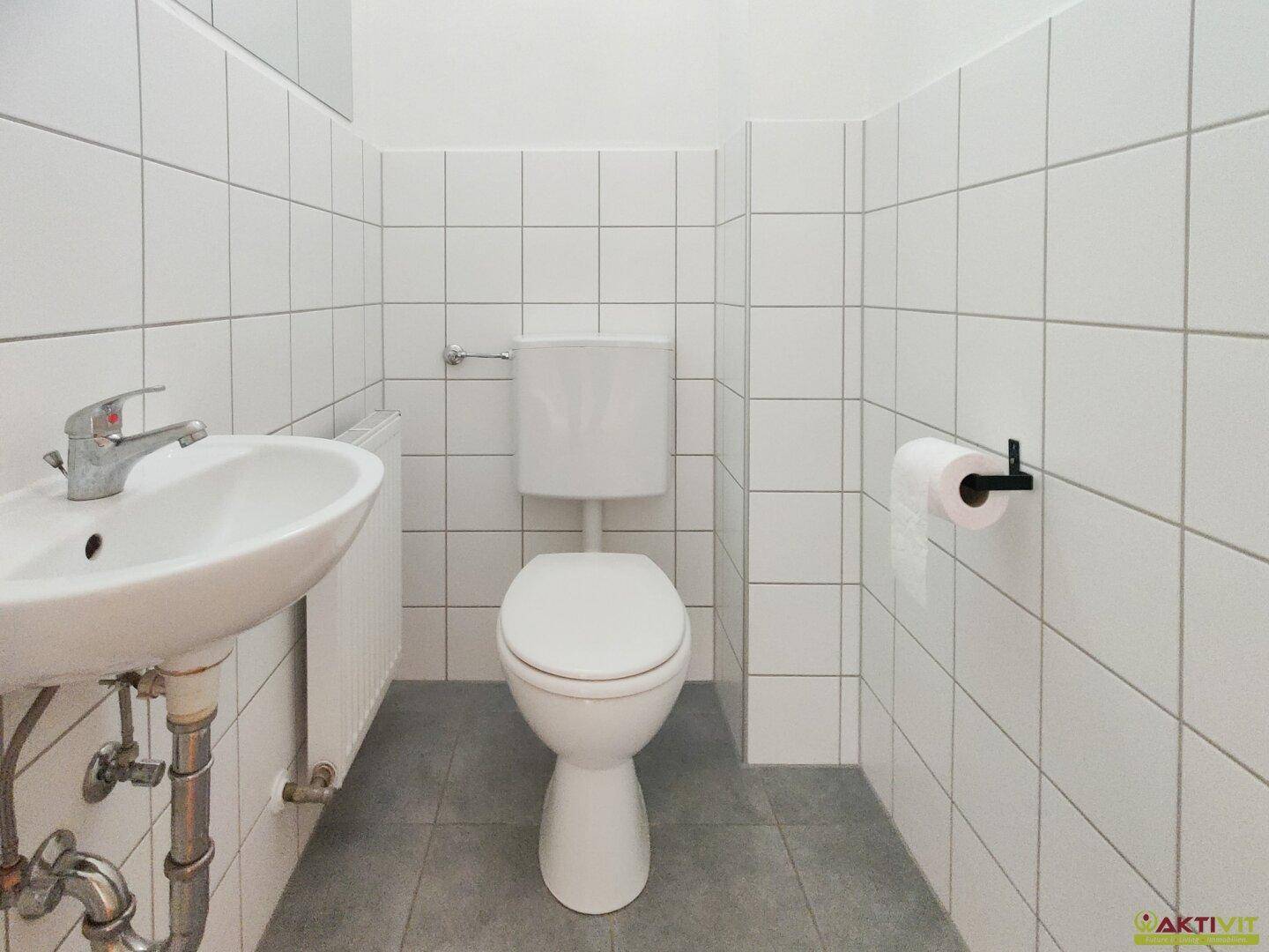 Modern gefliestes Gäste-WC mit weißer Toilette und Waschbecken, sauber und funktional.