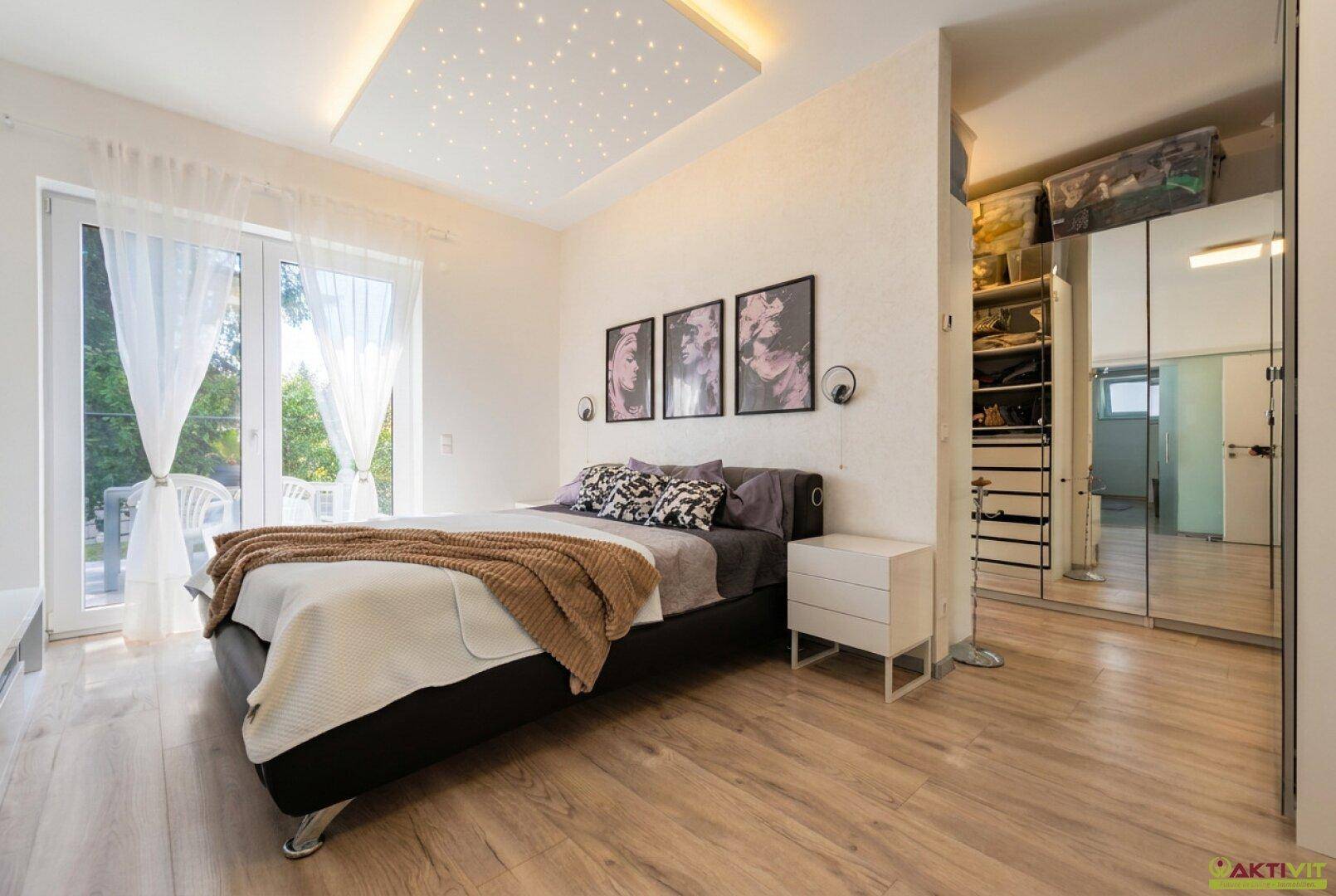 Helles Schlafzimmer mit Holzboden, großem Bett und Zugang zum Ankleidezimmer.
