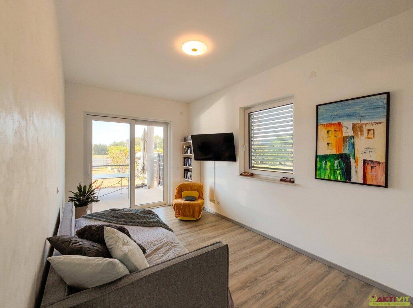 Helles Gästezimmer mit Holzboden, großem Fenster und Zugang zur Terrasse.