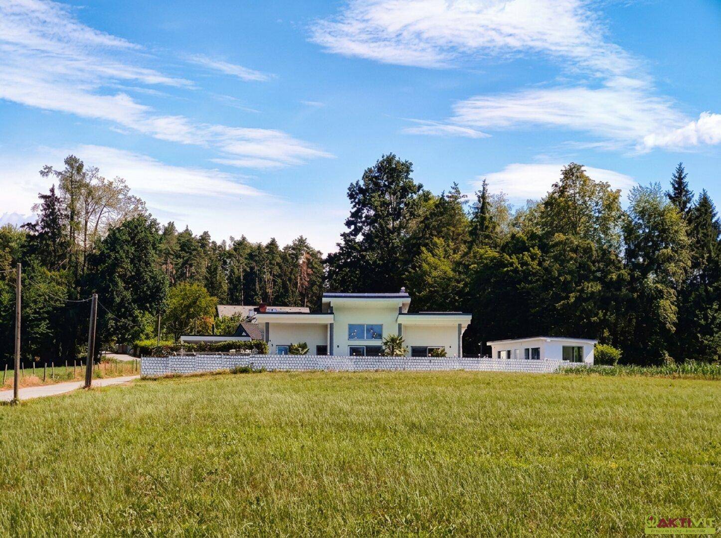 Modernes Wohnhaus in ländlicher Umgebung, umgeben von weiten Feldern und Bäumen.