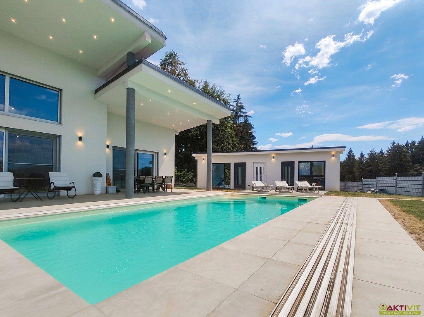 Großer Außenpool mit Liegeflächen und überdachtem Terrassenbereich am modernen Haus.