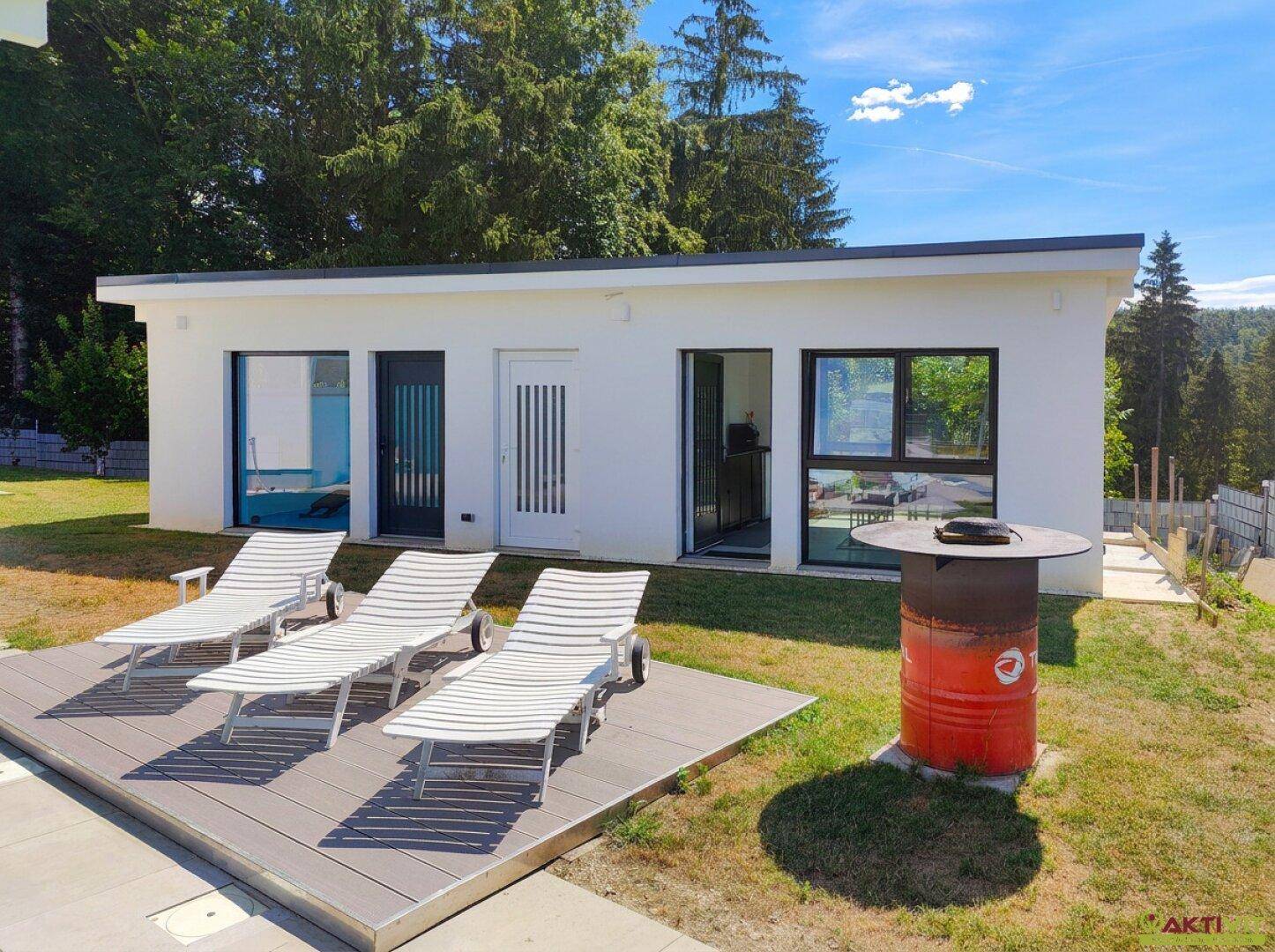 Entspannungsbereich mit Sonnenliegen auf einer Holzterrasse neben einem modernen Gebäude.