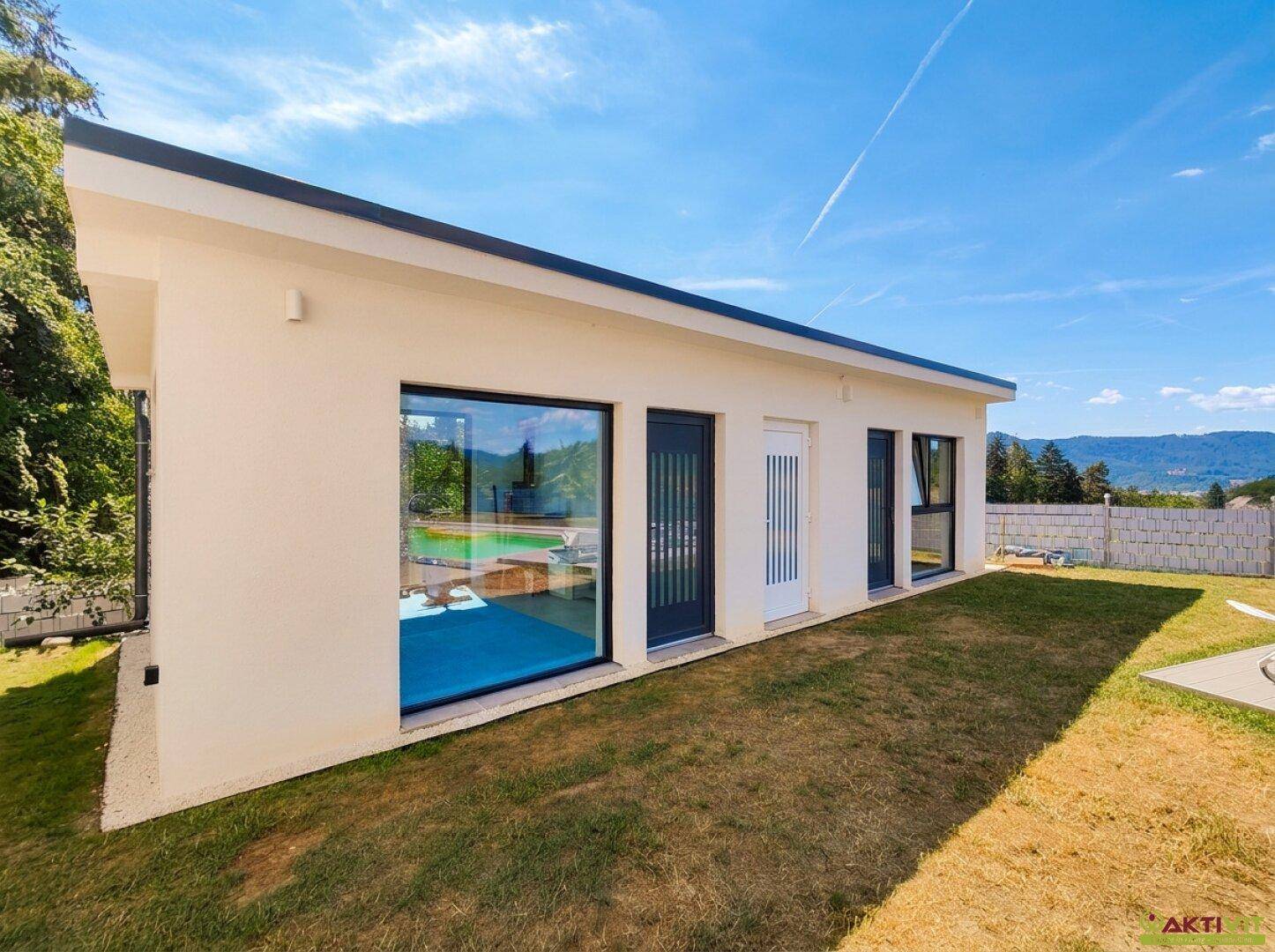 Modernes Nebengebäude mit großen Fenstern und gepflegtem Rasen unter blauem Himmel.