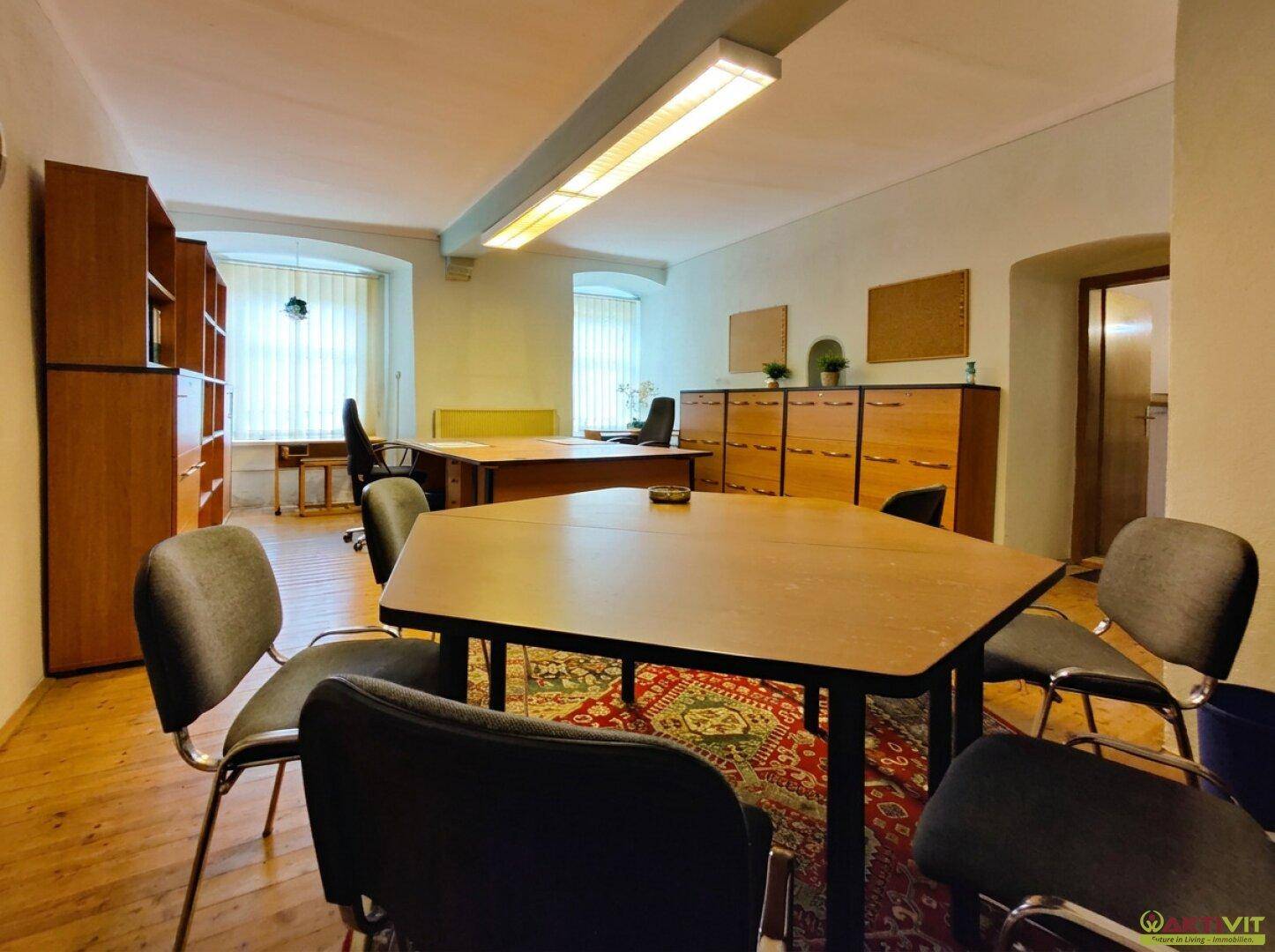 Geräumiges Büro mit mehreren Arbeitsplätzen, Holzmöbeln und Teppich auf Holzboden.