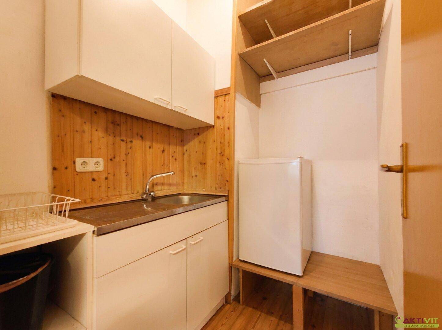 Kleine Küchenzeile mit Spüle, weißen Schränken und Kühlschrank in Holzvertäfelung.
