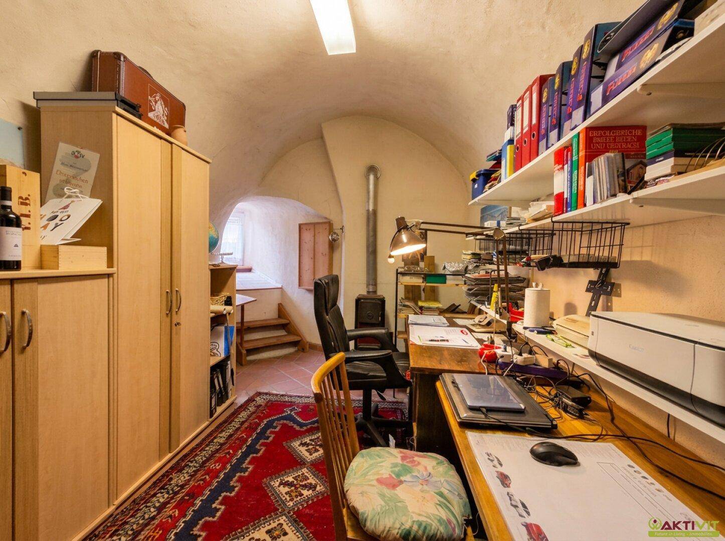 Arbeitszimmer mit gewölbter Decke, Schreibtisch, Regalen und Teppich auf dem Boden.