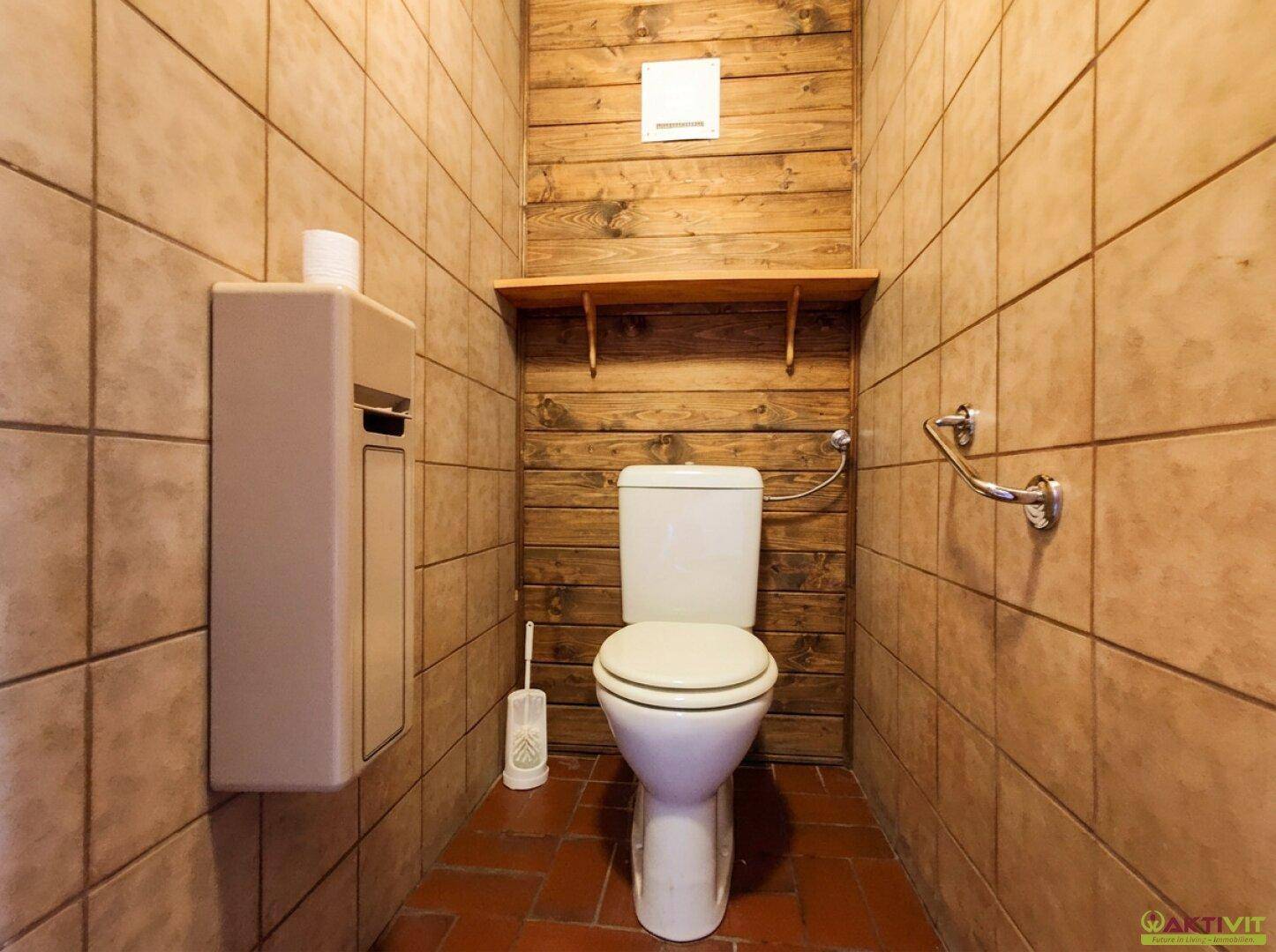 Kleines WC mit Fliesenboden, holzvertäfelter Wand und einfacher Toilette.