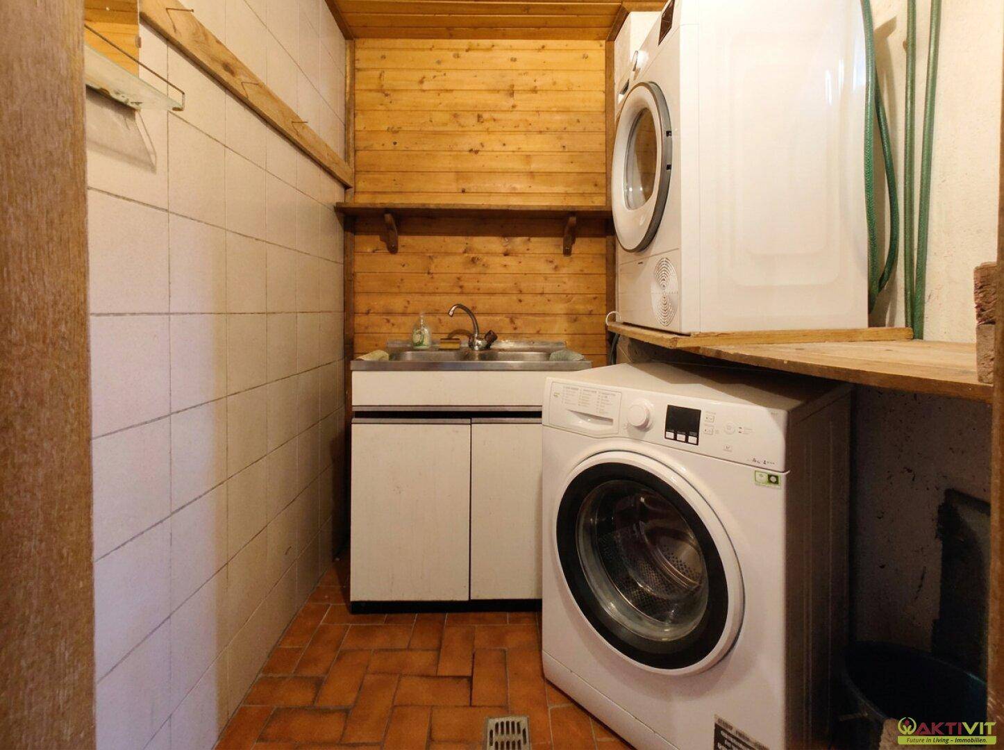 Hauswirtschaftsraum mit Waschmaschine, Trockner, Spülbecken und Fliesenboden.