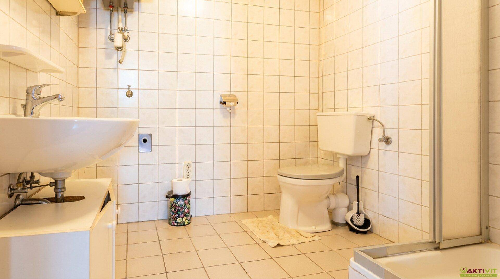 Helles Badezimmer mit weißen Fliesen, WC, Waschbecken und Duschkabine.