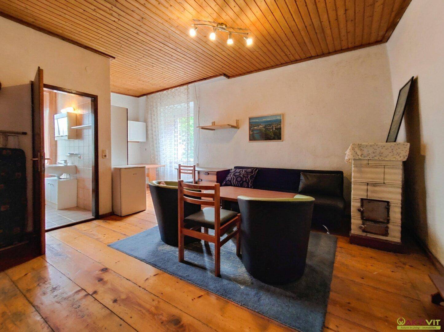 Gemütliches Wohnzimmer mit Kachelofen, Holzboden und Holzdecke, sowie Zugang zum Bad.