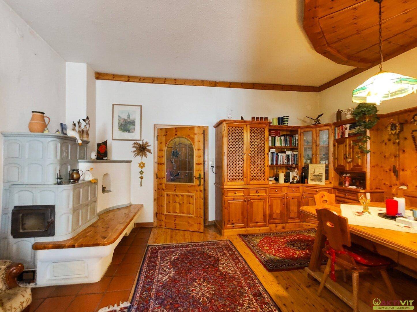 Esszimmer mit Kachelofen, Holztisch und Stühlen, umgeben von traditionellen Holzmöbeln.