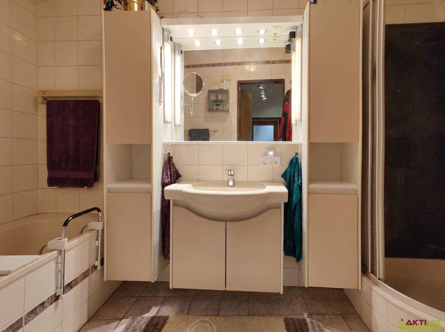 Badezimmer mit Waschbecken, Spiegelschrank, Badewanne und Duschkabine in hellen Fliesen.