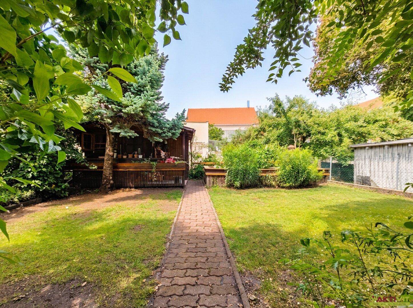 Gepflegter Garten mit Rasenfläche, gepflastertem Weg und einem Gartenhaus im Hintergrund.