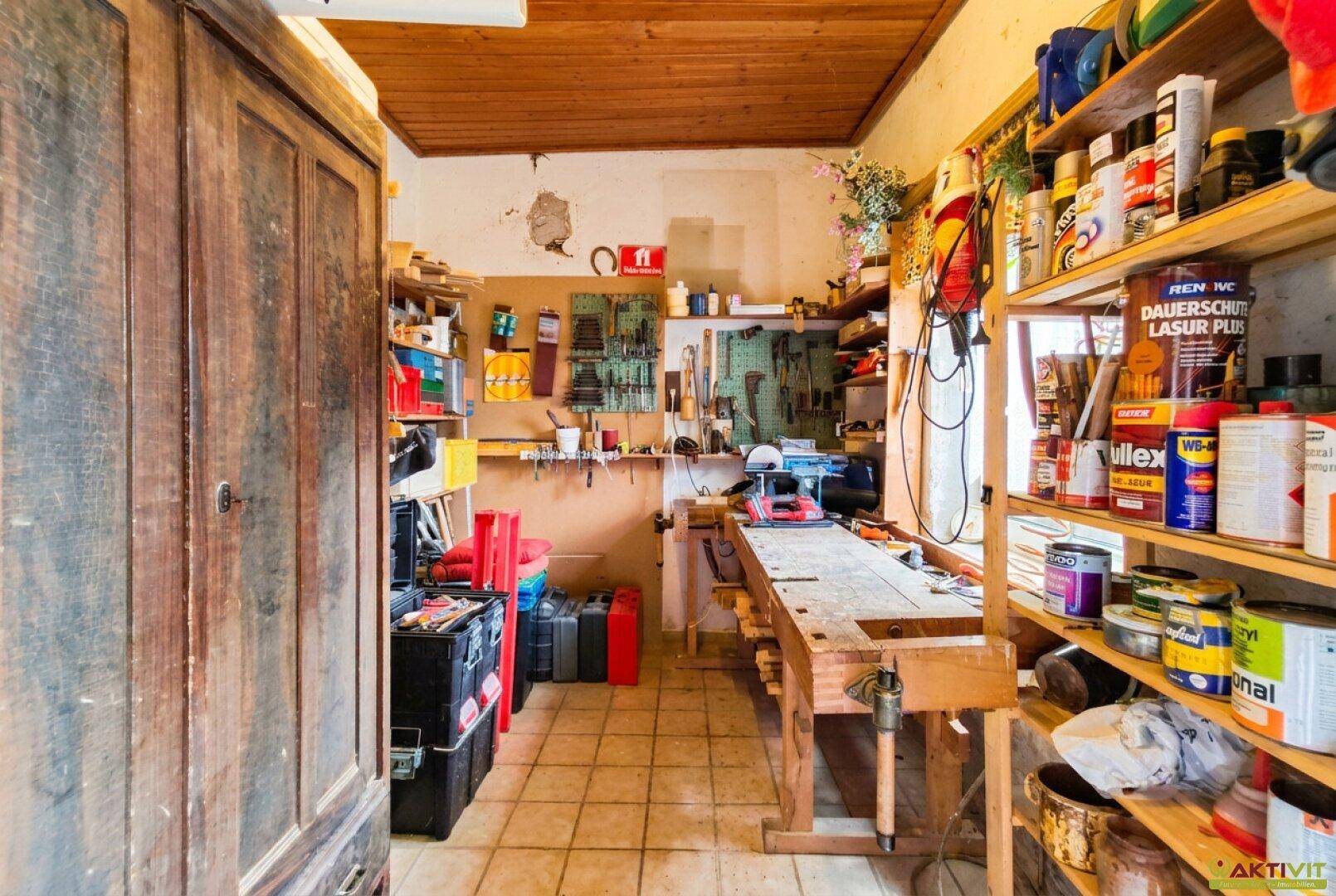 Gut ausgestattete Werkstatt mit Werkbank, Regalen und Holzdecke für Heimwerker.