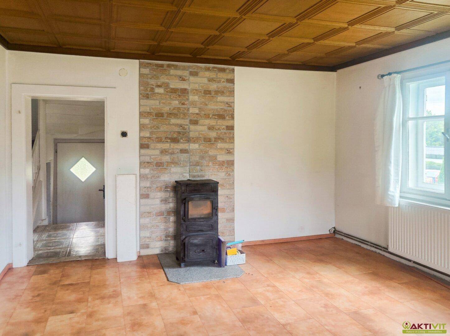 Wohnzimmer mit Kaminofen, Fliesenboden und Holzdeckenverkleidung.