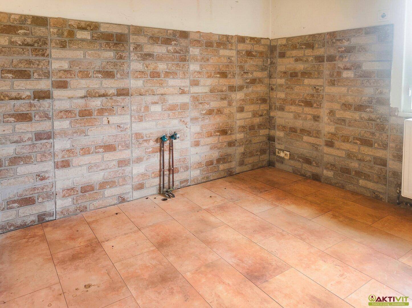 Leere Küche mit Ziegelwandfliesen und sichtbaren Wasseranschlüssen.