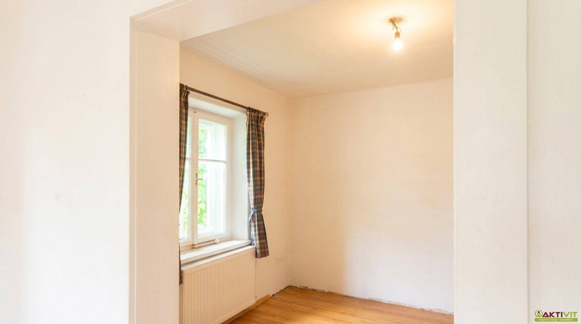 Helles Schlafzimmer mit Holzfußboden und Fenster mit Blick ins Grüne.