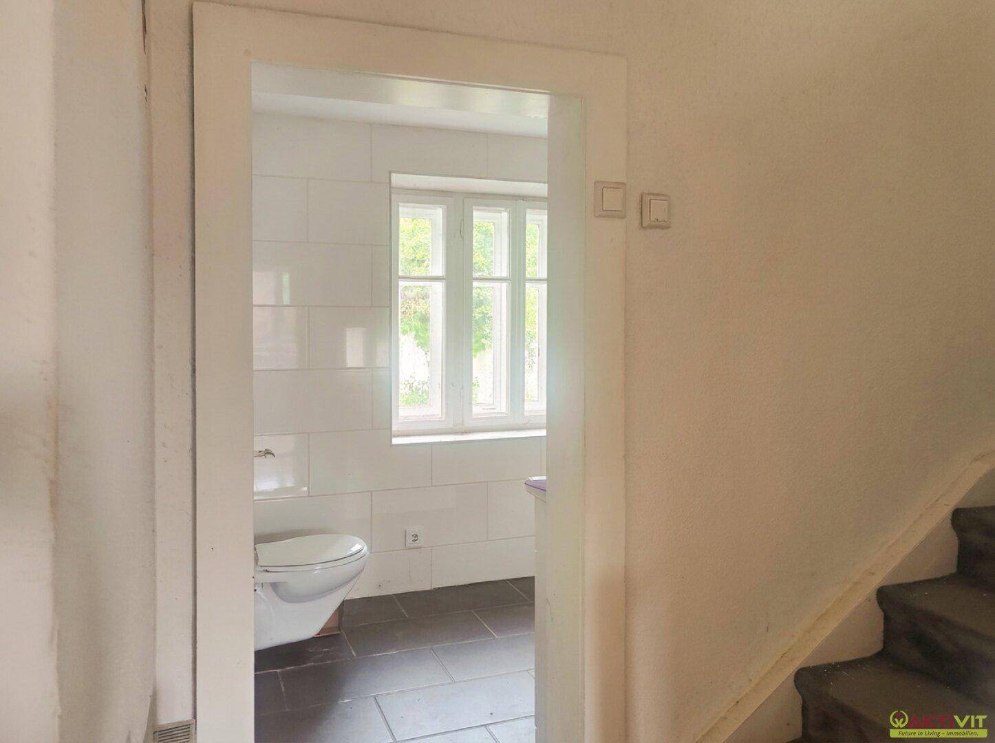 Separates WC mit Wand-WC, Fliesenboden und Fenster.
