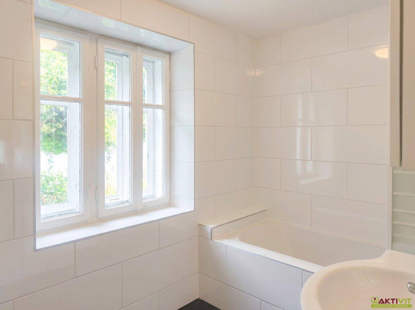 Badezimmer mit Badewanne, Waschbecken und großem Fenster.