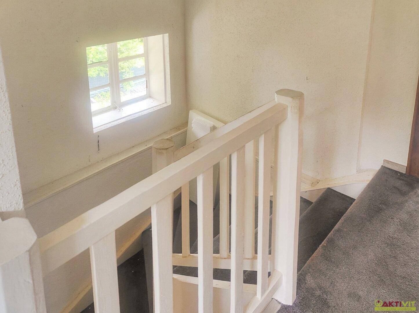 Treppenhaus mit Teppichboden und kleinem Fenster für natürliches Licht.