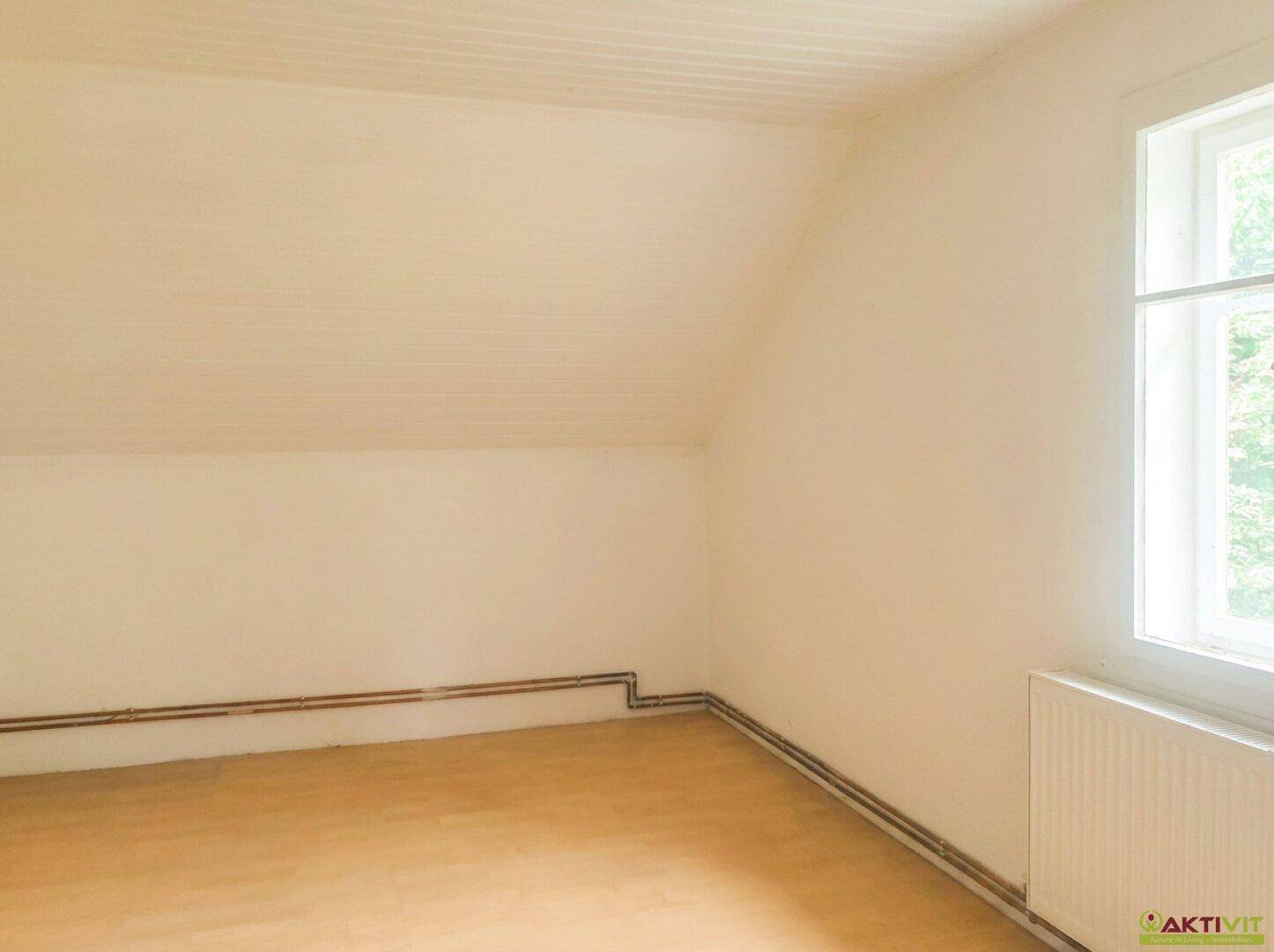 Schlafzimmer im Dachgeschoss mit schräger Decke, Holzfußboden und Fenster.