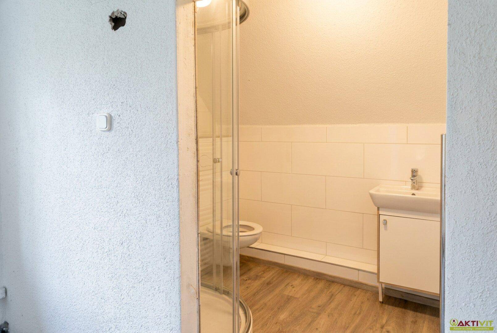 Badezimmer im Dachgeschoss mit Dusche, WC, Waschbecken und schräger Decke.