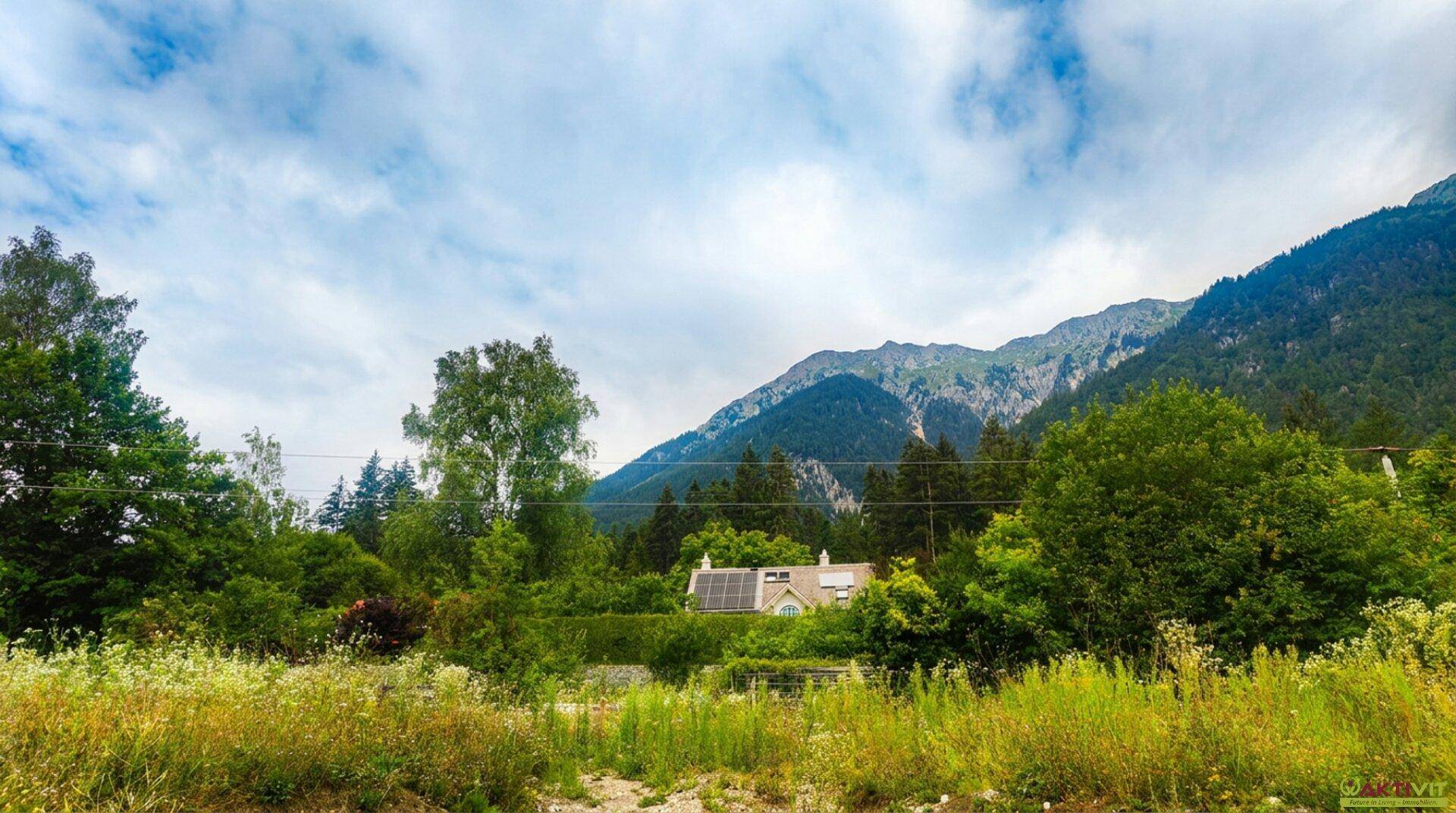 Weitläufige grüne Landschaft mit einem Haus, Solarpaneelen auf dem Dach und Bergblick.