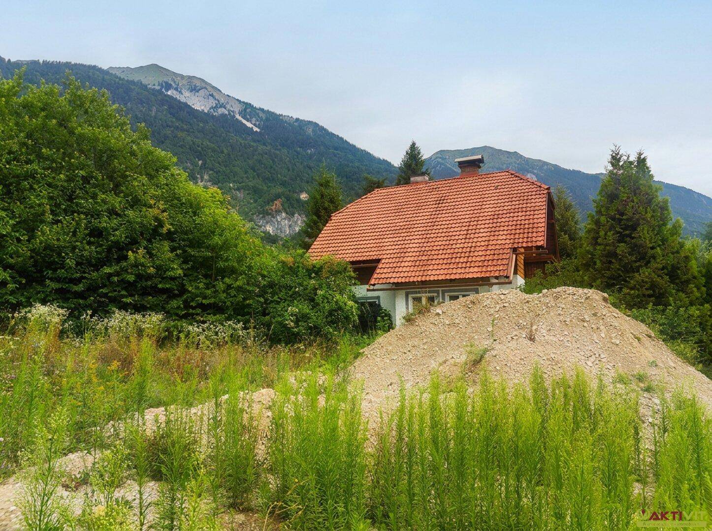 Traditionelles Haus mit rotem Ziegeldach, umgeben von üppigem Grün und einem Erdhaufen.