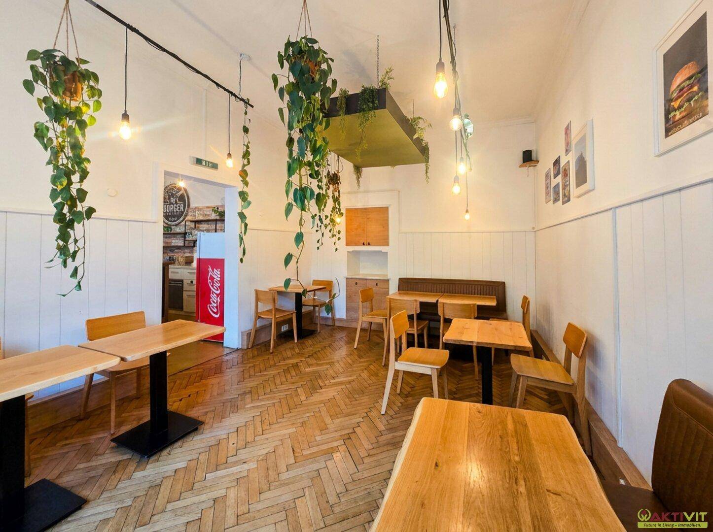 Geräumiger Essbereich mit Holztischen, Stühlen und Fischgrätparkett, dekoriert mit hängenden Pflanzen.