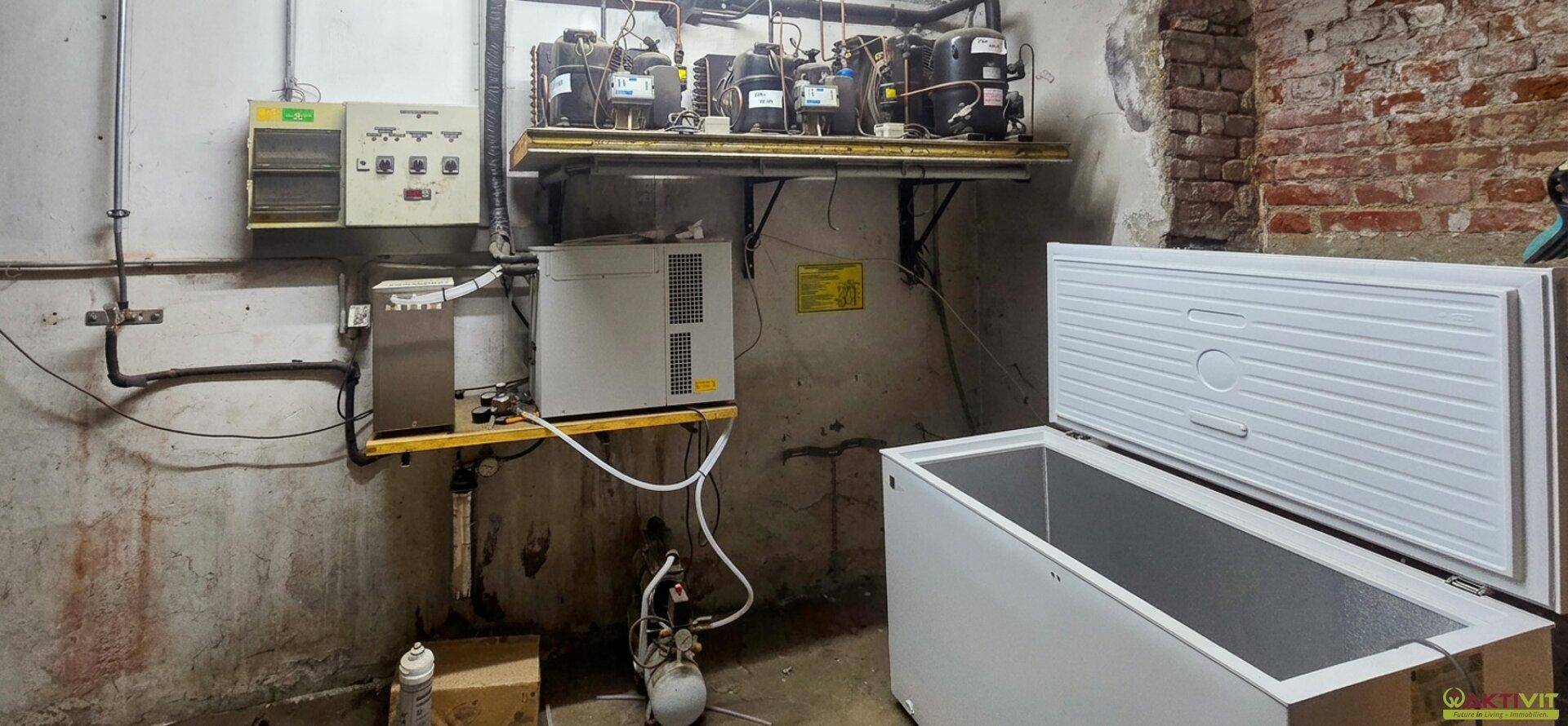 Kellerraum mit industriellen Kühlanlagen, freiliegenden Ziegelwänden und einer großen Gefriertruhe.