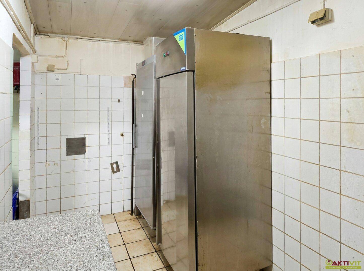 Lagerraum mit großen Edelstahlkühlschränken und gefliesten Wänden, ideal für die Lebensmittelaufbewahrung.