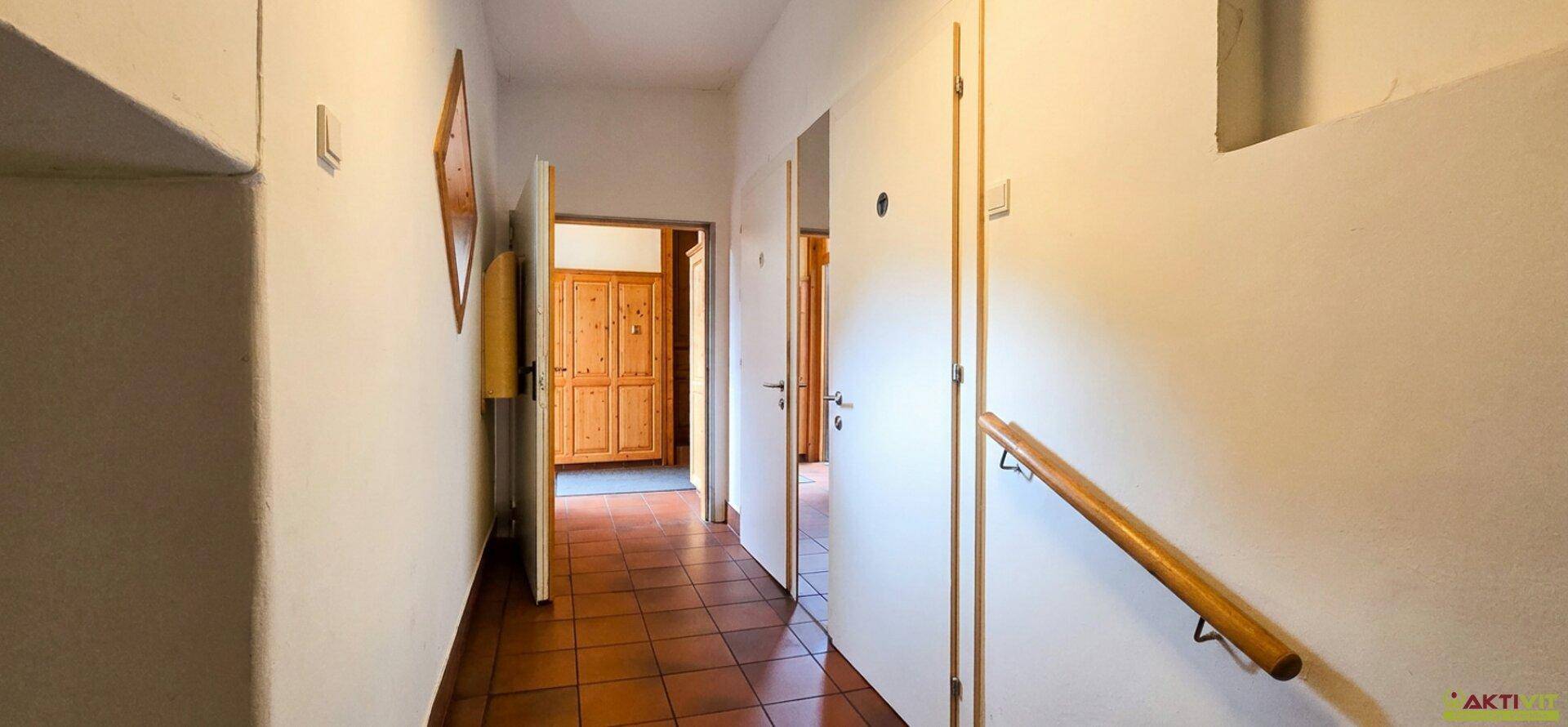 Flur mit Holzhandlauf und terrakottafarbenen Fliesen, der zu mehreren Räumen führt.
