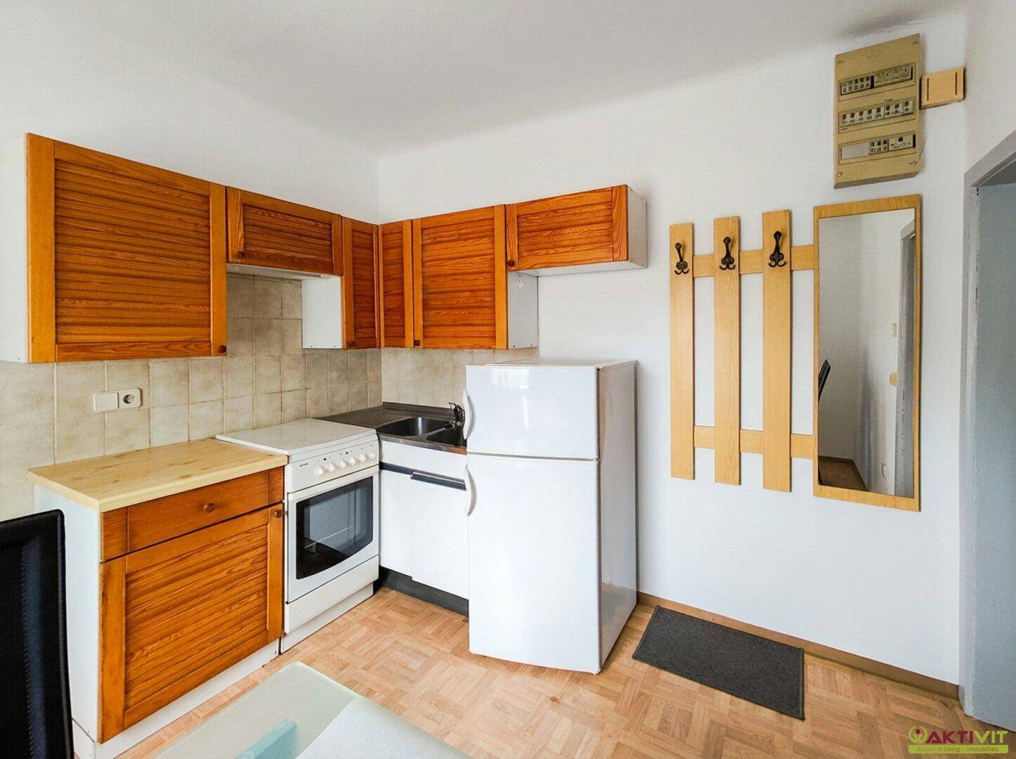 Kleine Küchenzeile mit Holzschränken, Herd, Spüle und Kühlschrank in einem funktionalen Raum.