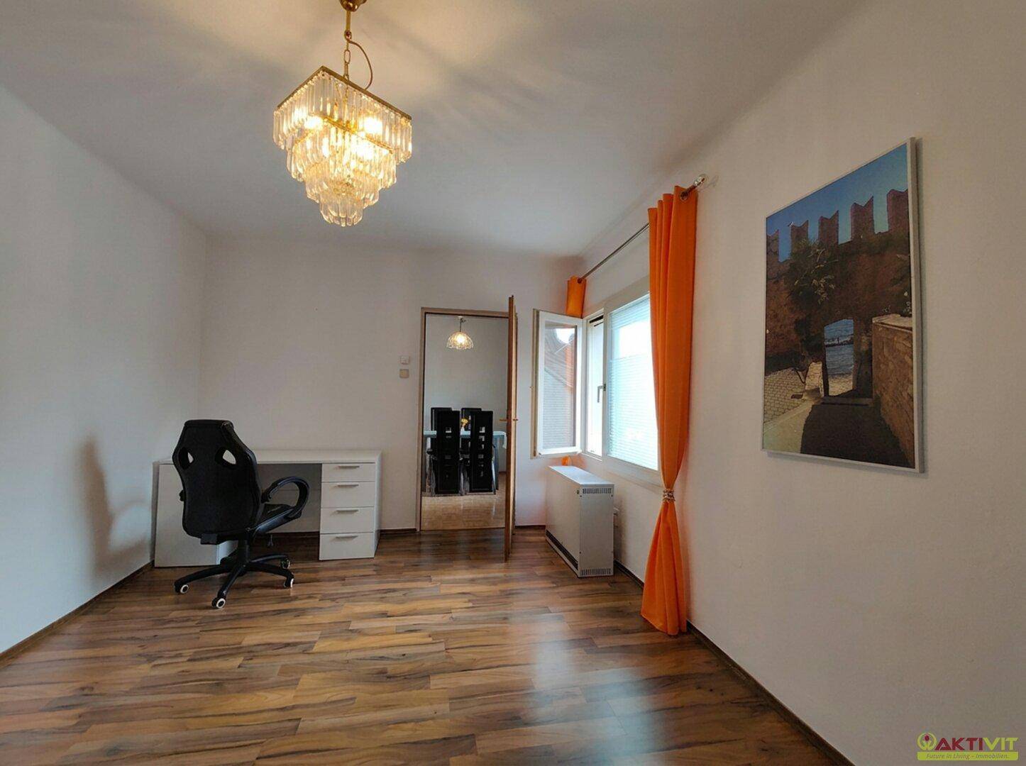 Geräumiger Raum mit Holzboden, Schreibtisch und einem eleganten Kronleuchter, ideal als Büro.