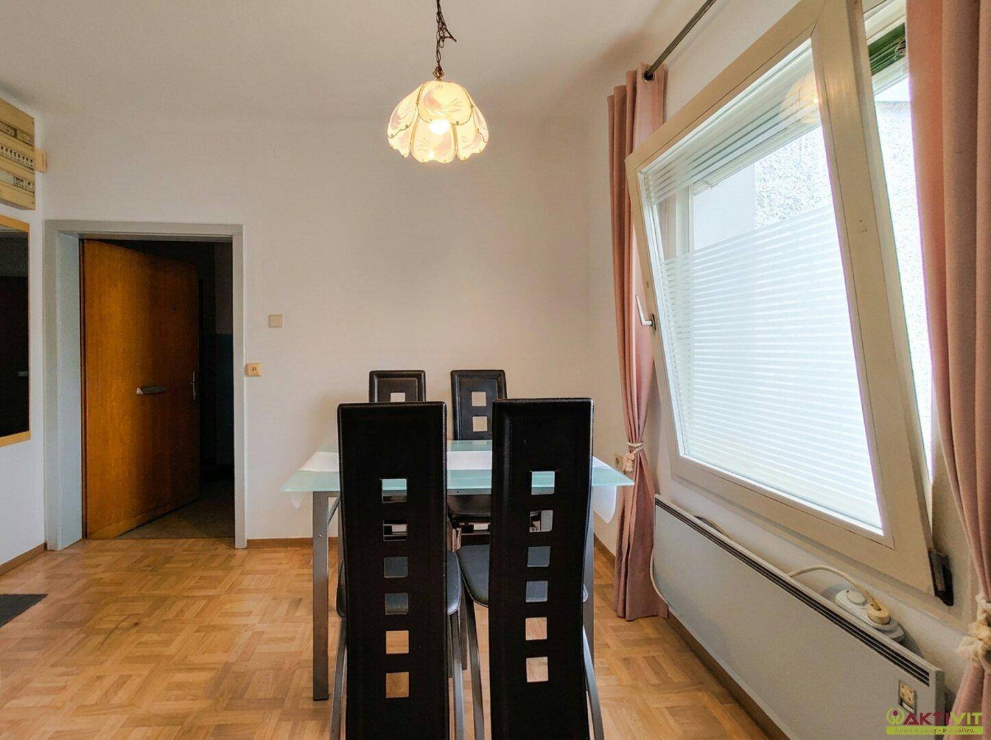 Heller Essbereich mit modernem Glastisch, dunklen Stühlen und Parkettboden.