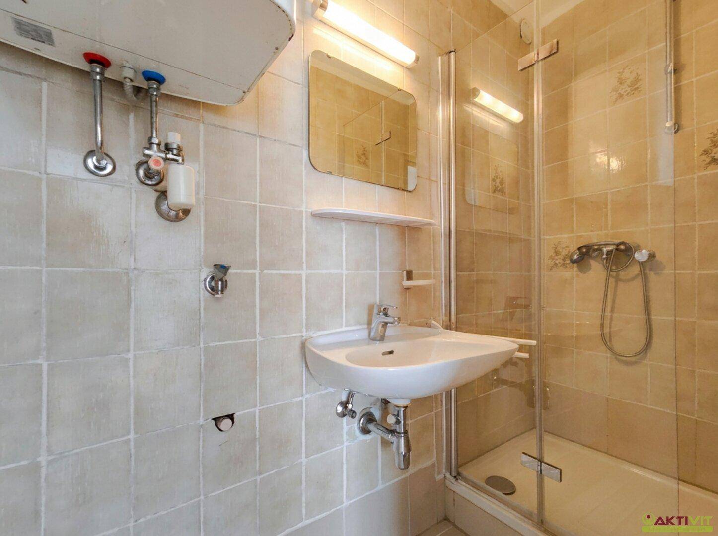 Kleines Badezimmer mit Duschkabine, Waschbecken und beigefarbenen Fliesen im 80er-Jahre-Stil.