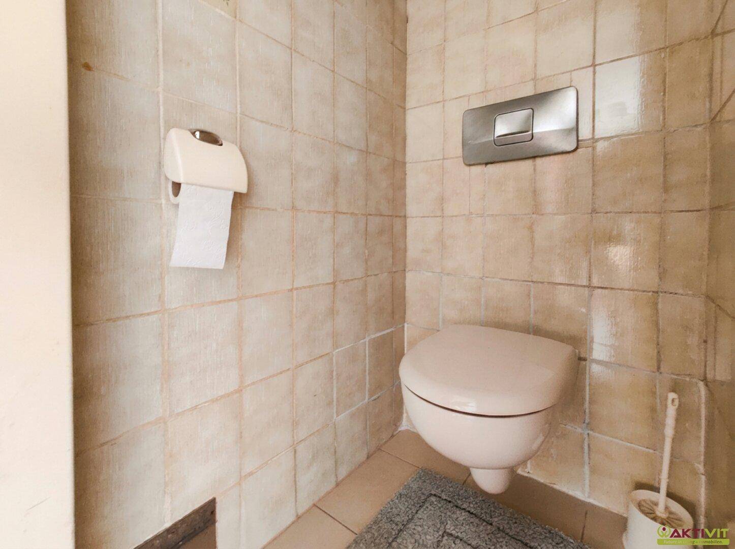 Separate Toilette mit beigefarbenen Fliesen und Wand-WC im 80er-Jahre-Stil.