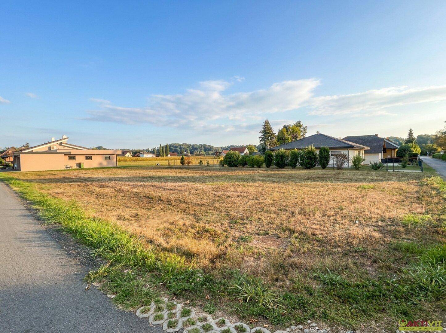 Sonniges Grundstück mit trockenem Gras und Blick auf die umliegende Landschaft und Häuser.