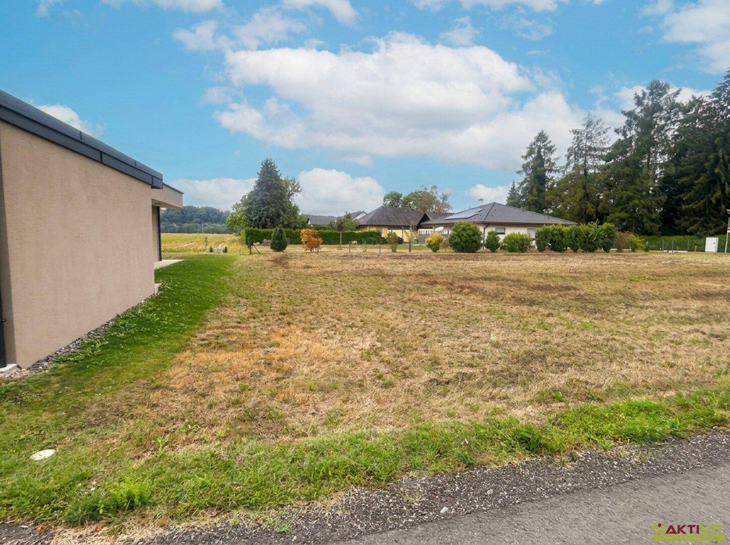 Freies Grundstück mit trockenem Gras und angrenzendem Gebäude unter blauem Himmel.