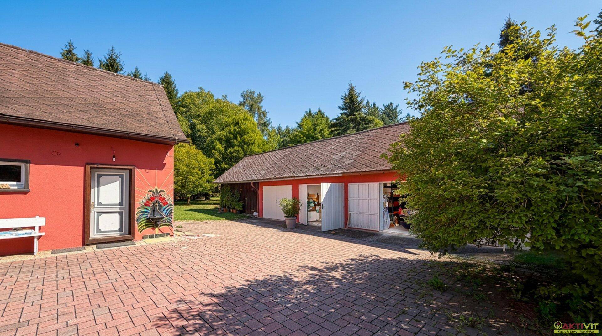 Weitläufiger Außenbereich mit rotem Hauptgebäude, separater Garage und gepflastertem Hof.