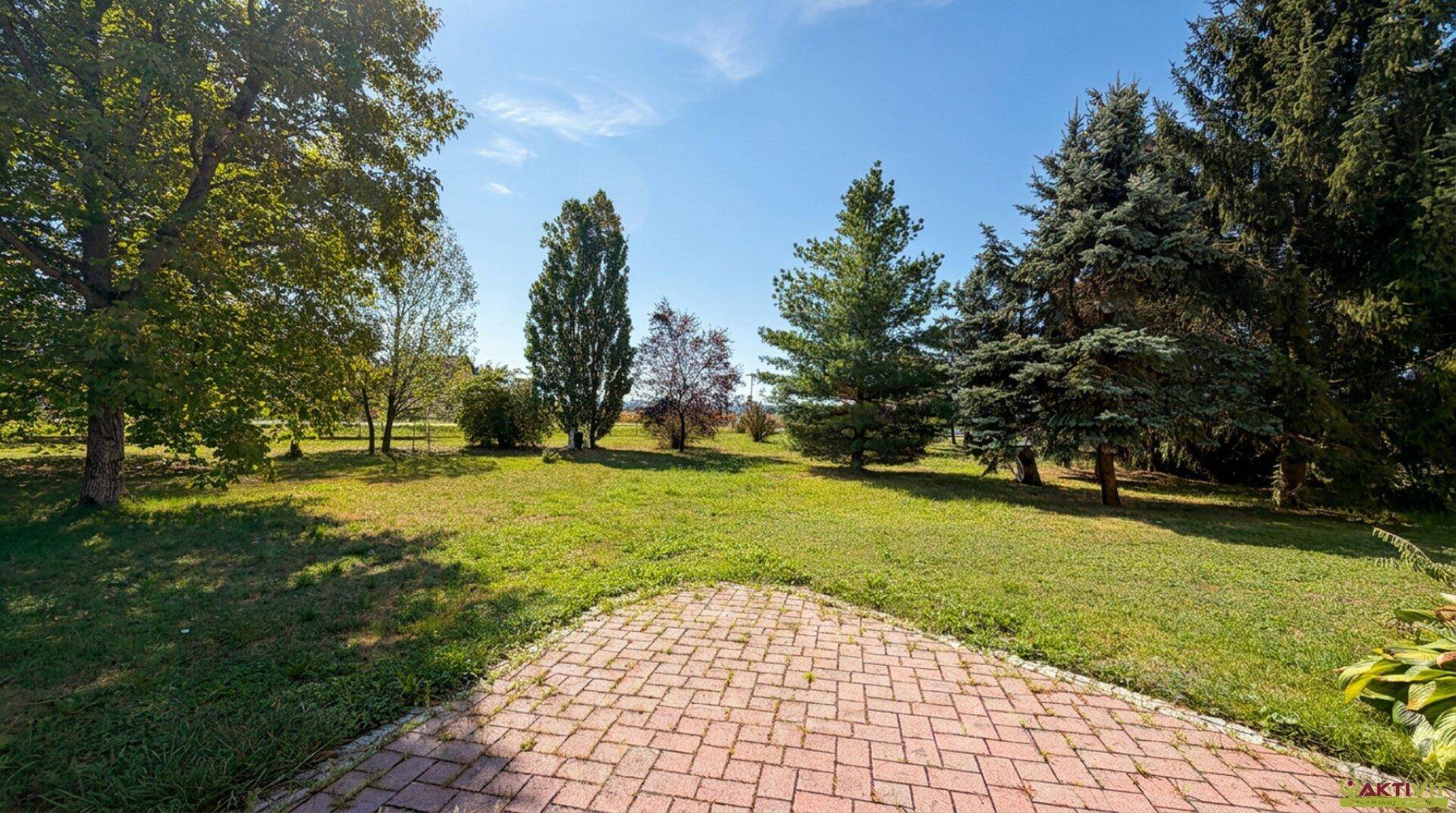 Weitläufiger Garten mit Rasenfläche, alten Bäumen und freiem Blick auf die umliegende Landschaft.