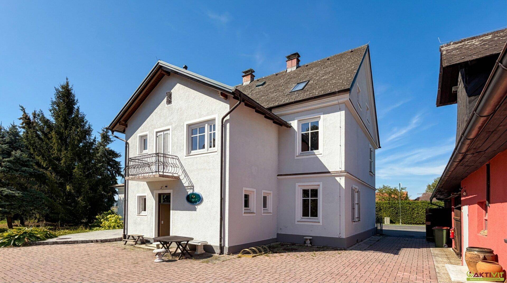 Traditionelles Wohnhaus mit weißer Fassade, kleinen Balkonen und gepflastertem Vorplatz.