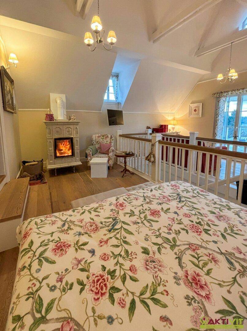 Helles Schlafzimmer im Dachgeschoss mit Kamin, Holzboden und floraler Bettwäsche.