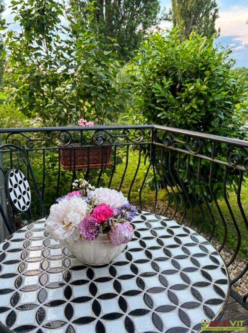 Kleiner Balkon mit Mosaiktisch, Blumen und Blick ins Grüne.