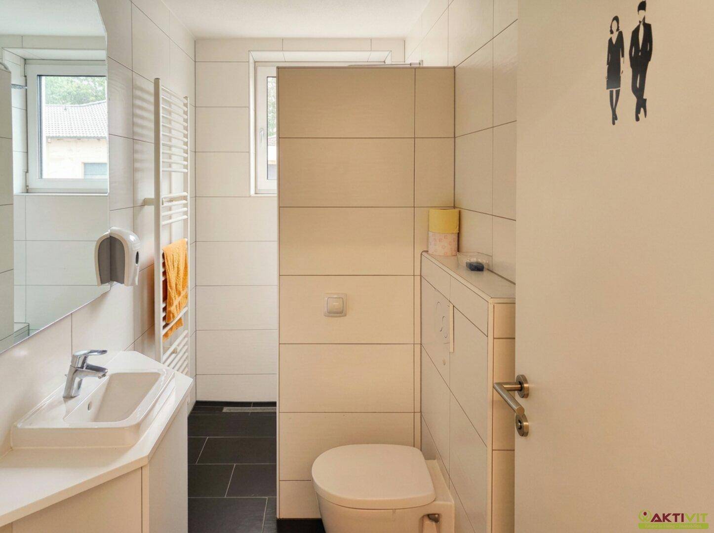 Modernes Gäste-WC mit weißen Fliesen, Einzelwaschbecken und Fenster für Tageslicht.