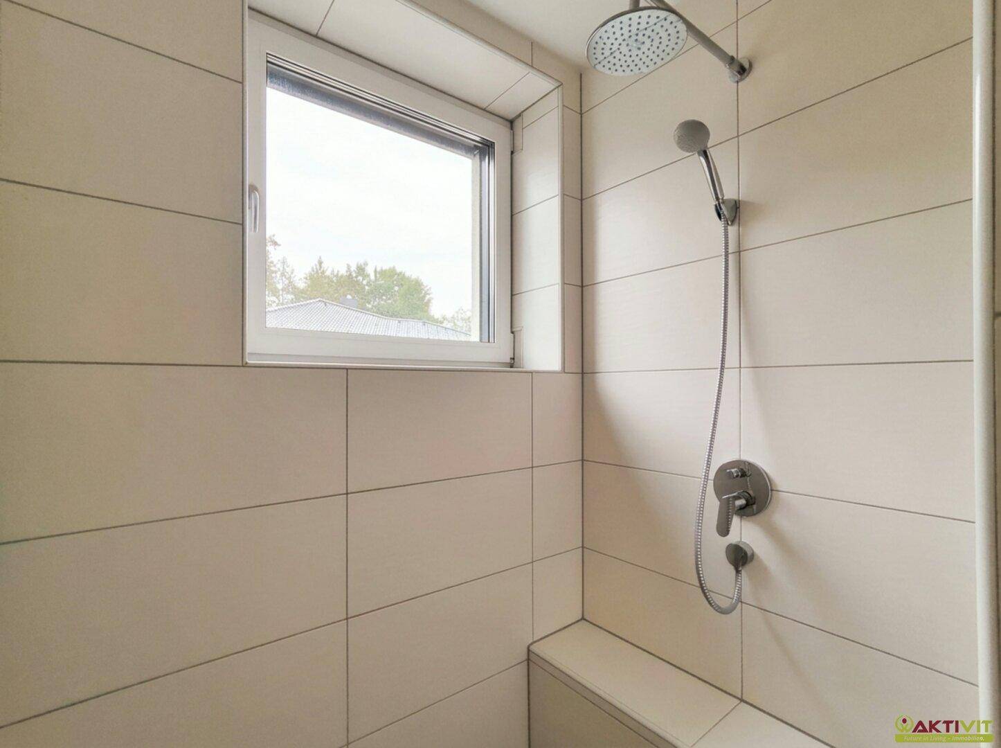 Moderne Dusche mit Regenduschkopf und Handbrause in einem hell gefliesten Badezimmer.