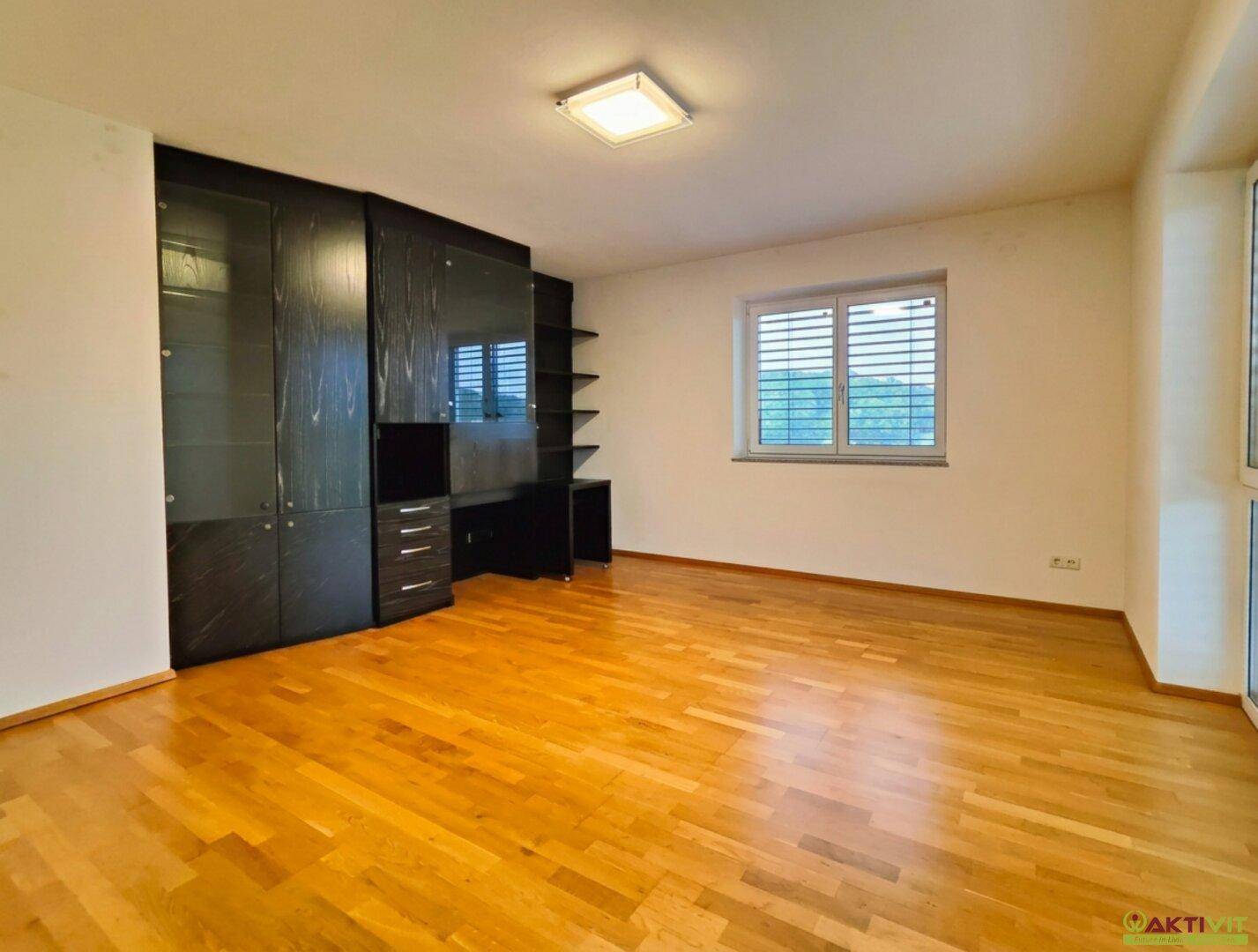 Helles Schlafzimmer mit Holzboden, großem Einbauschrank und Fenster mit Blick ins Grüne.